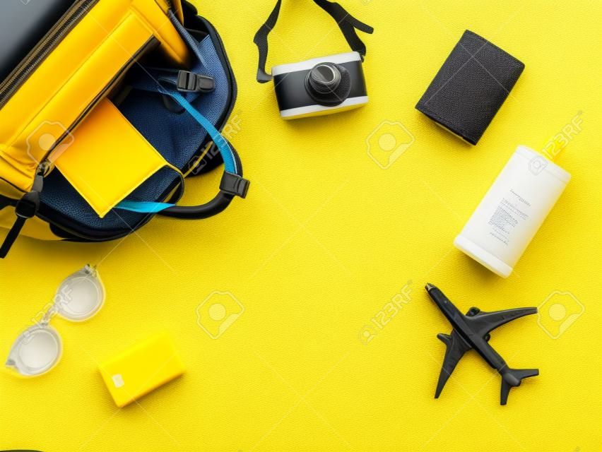 Vista dall'alto o disposizione piatta degli accessori da viaggio con maschera medica e spray alcolico nello zaino su sfondo giallo. Viaggiare durante la pandemia e la nuova normalità.