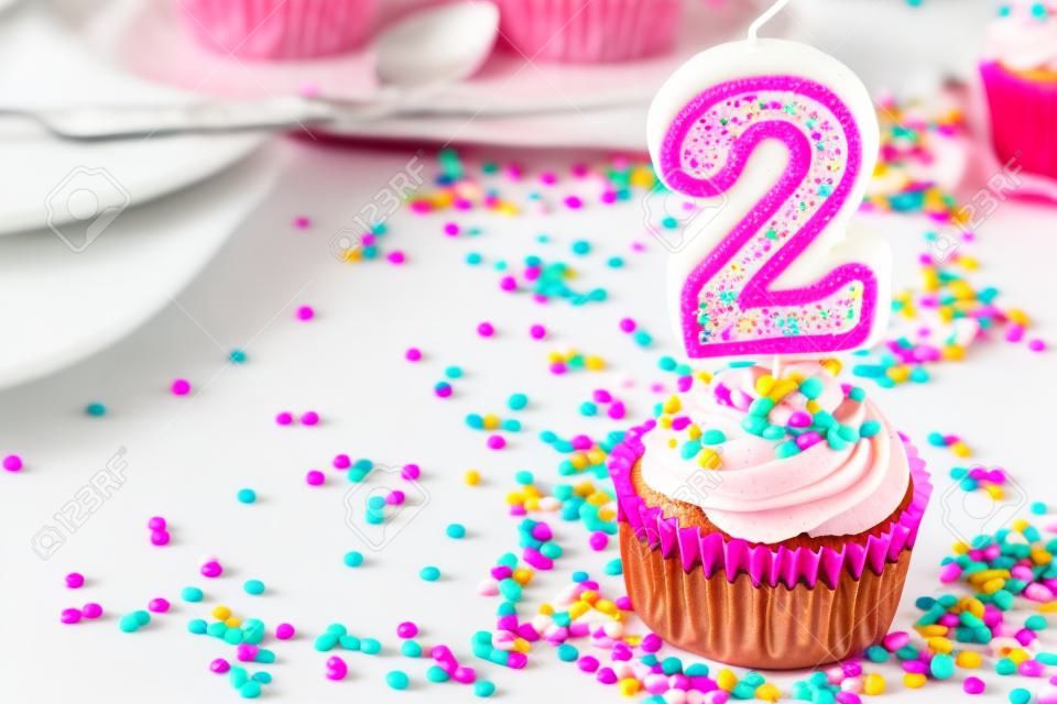 Petit gâteau avec le glaçage rose et arrose et une 2ème bougie d'anniversaire
