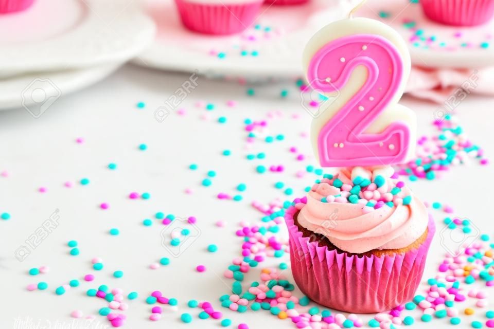 Petit gâteau avec le glaçage rose et arrose et une 2ème bougie d'anniversaire