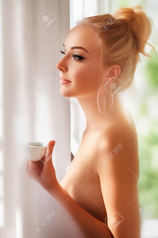 Portrait of the beautiful woman. She is drinking tea at the window