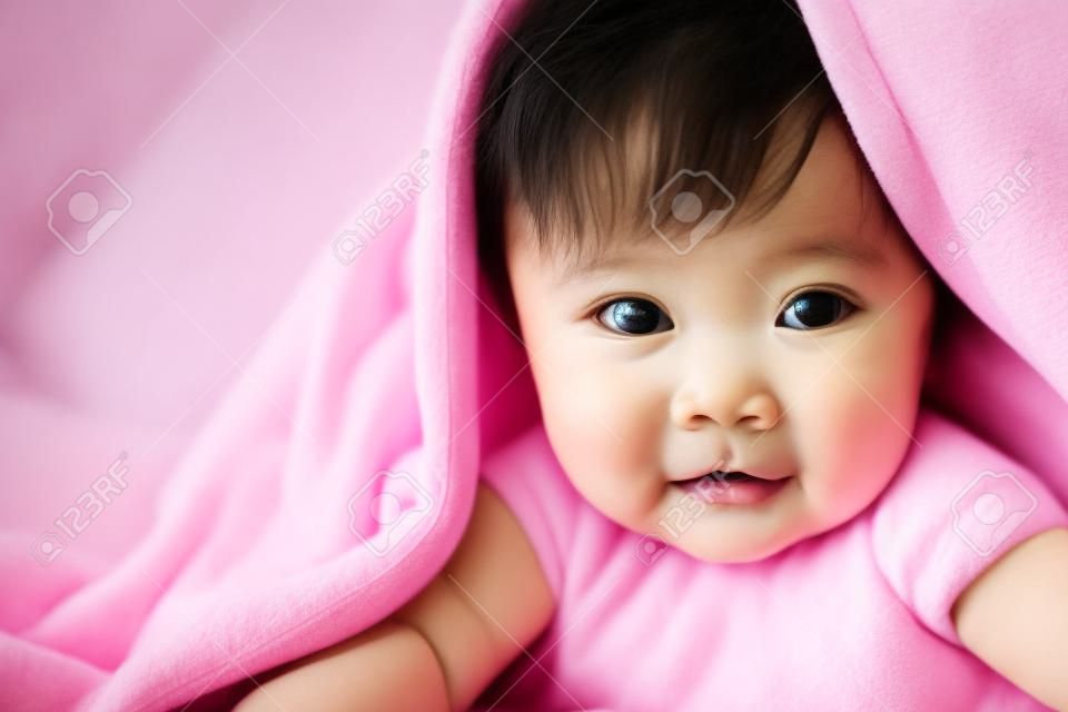 schattig aziatisch baby meisje glimlachen onder roze deken en liggen op haar buik op het bed