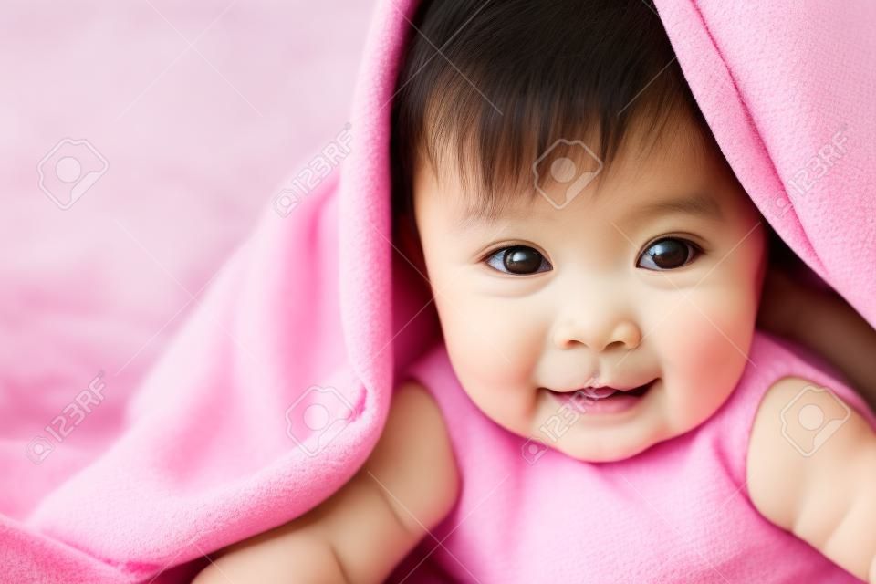 schattig aziatisch baby meisje glimlachen onder roze deken en liggen op haar buik op het bed