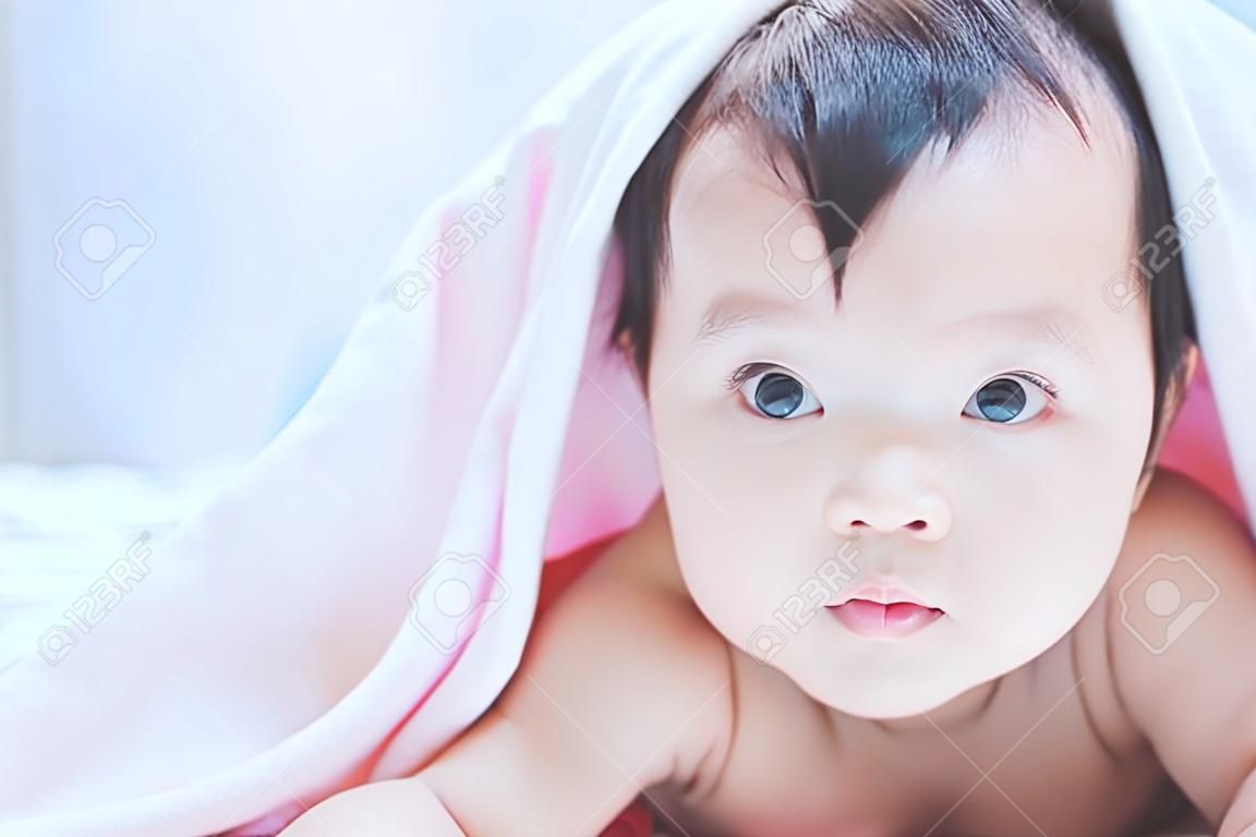 Neonata asiatica sveglia che sorride sotto la coperta rosa e che si trova sul suo stomaco sul letto