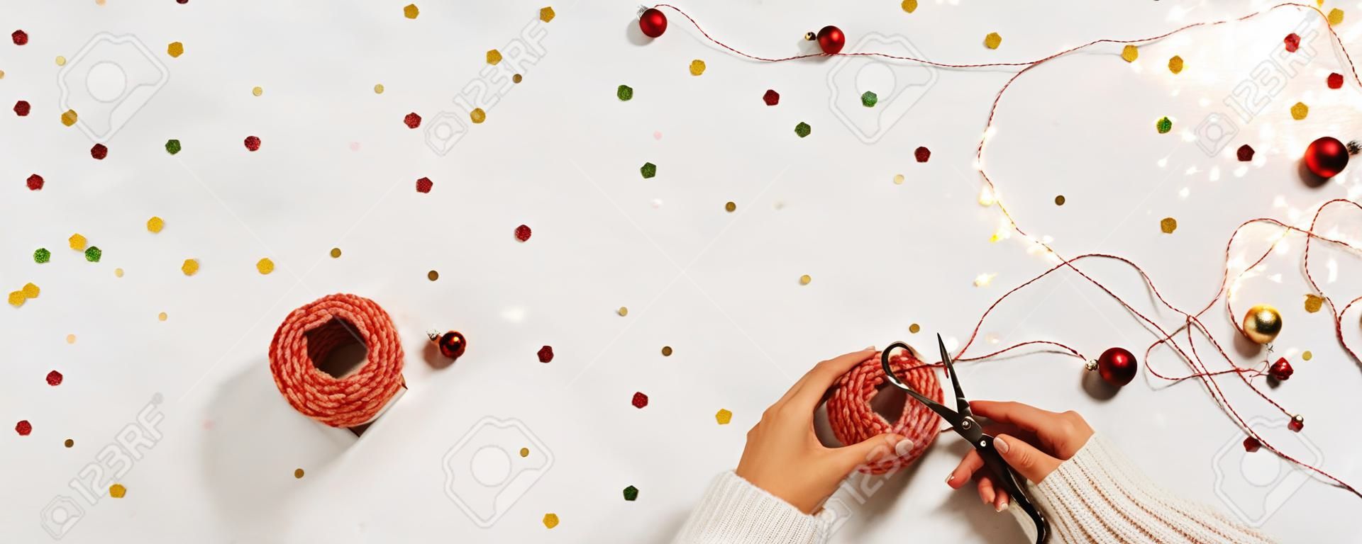 Frauenhände in einem Pullover packen eine Geschenkbox für das neue Jahr. Kreatives Weihnachtslayout auf weißem Hintergrund mit Konfetti und Platz für Text.