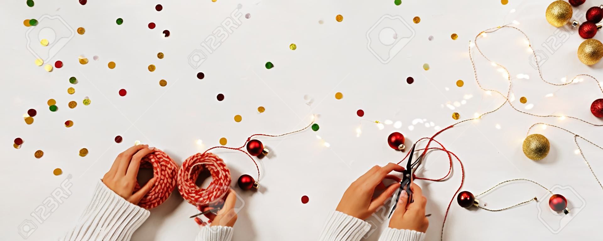 Frauenhände in einem Pullover packen eine Geschenkbox für das neue Jahr. Kreatives Weihnachtslayout auf weißem Hintergrund mit Konfetti und Platz für Text.