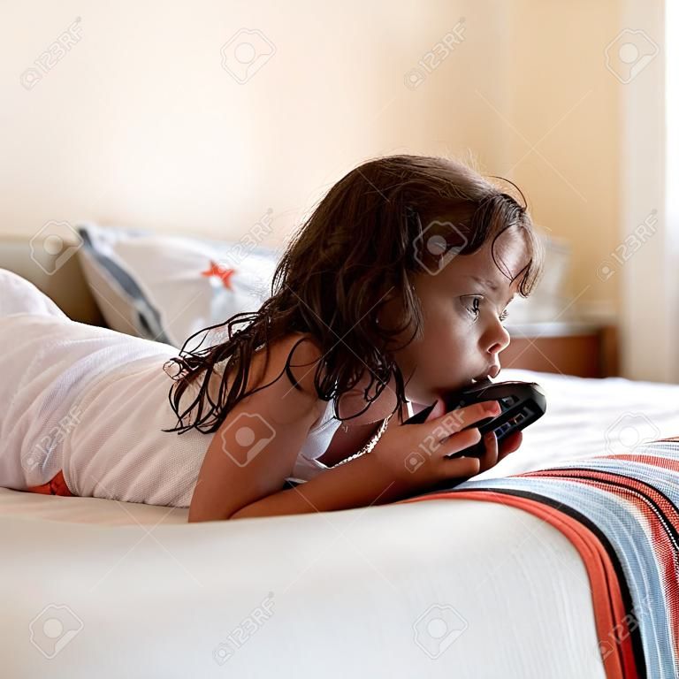 Bambina sdraiata sul letto a guardare la televisione