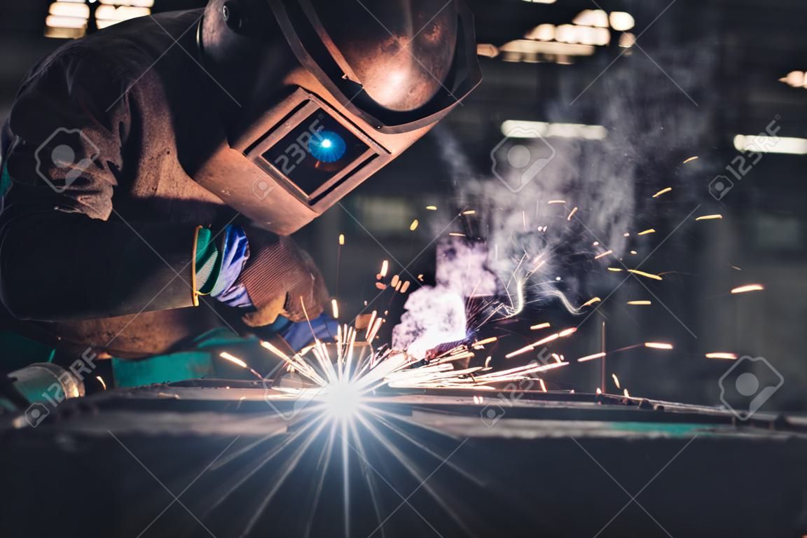 Geschickter Metallarbeiter, der mit einer Lichtbogenschweißmaschine in der Fabrik arbeitet, während er Sicherheitsausrüstung trägt. Herstellung von Metallarbeiten und Bauwartungsservice durch manuelles Facharbeitskonzept.