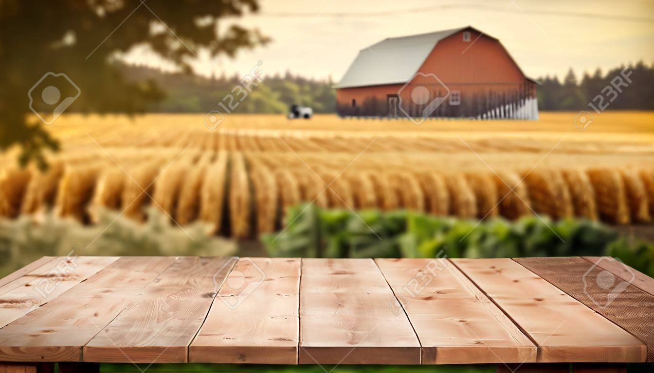 La mesa marrón de madera vacía con fondo borroso de imagen exuberante de granja y granero