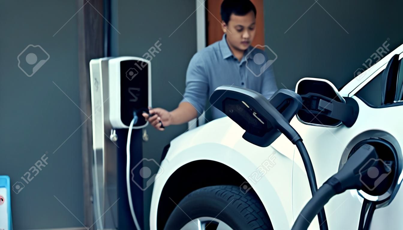 A man unplugs the electric vehicles charger at his residence. Concept of the use of electric vehicles in a progressive lifestyle contributes to a clean and healthy environment.