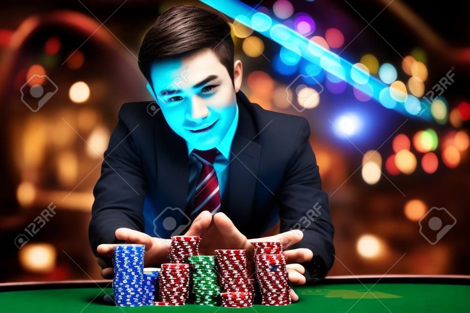 Porträt benutzte der junge Spielermann die Hände, die großen Stapel der farbigen Spielertabelle der farbigen Schürhakenchips für das Wetten auf Kasinoclubhintergrund drücken