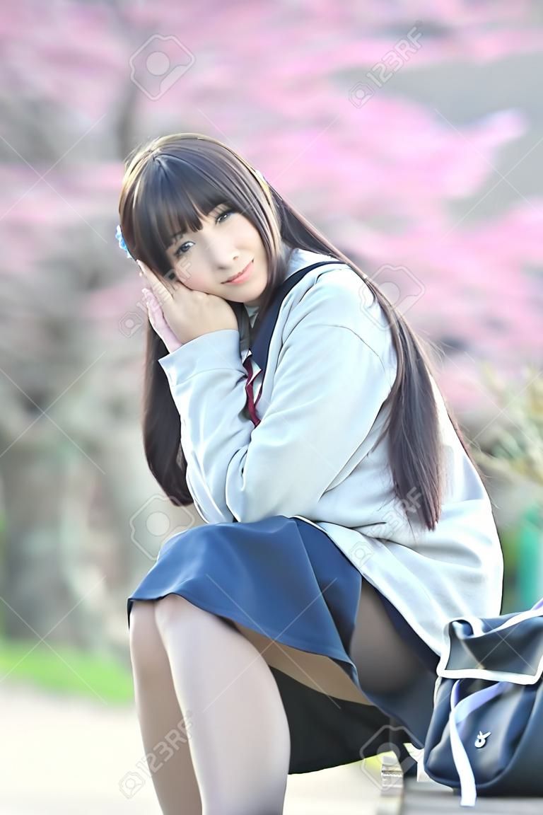 桜の花の自然歩道で座っている日本の女子校生ドレス