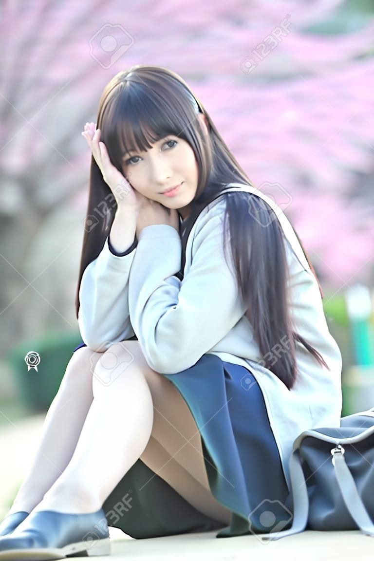 桜の花の自然歩道で座っている日本の女子校生ドレス