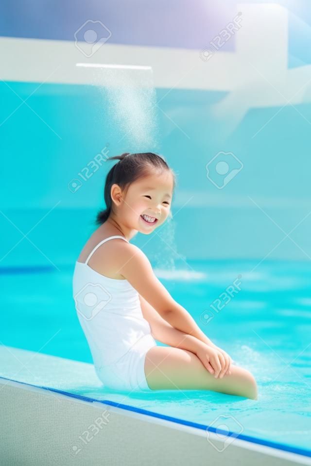 Happy little girl sitting by swimming pool stock photo