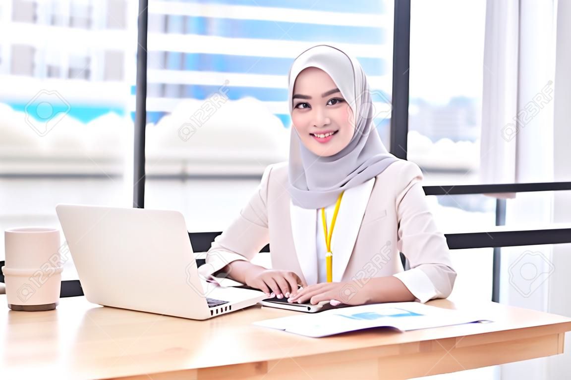 Fiducioso dirigente di donne d'affari musulmane dell'Asia (Islam) vestito con il velo religioso, lavorando nell'ufficio moderno e guardando la fotocamera e sorridere. Concetto di lavoro di diversità culturale.