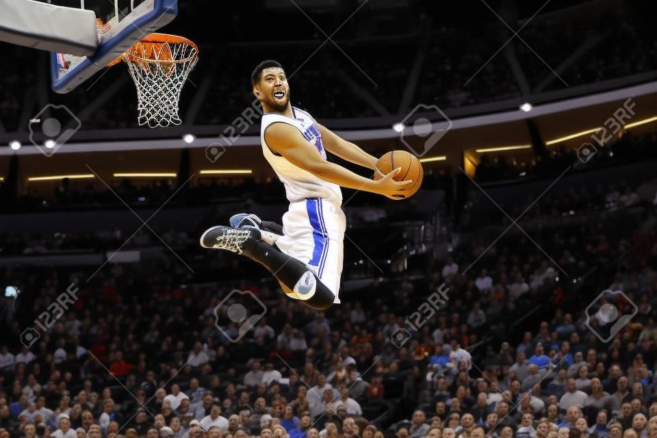 Foto orizzontale del giocatore di basket in gioco rende slam dunk inverso. NBA. Partita di pallacanestro. Sportivo gioca a basket.