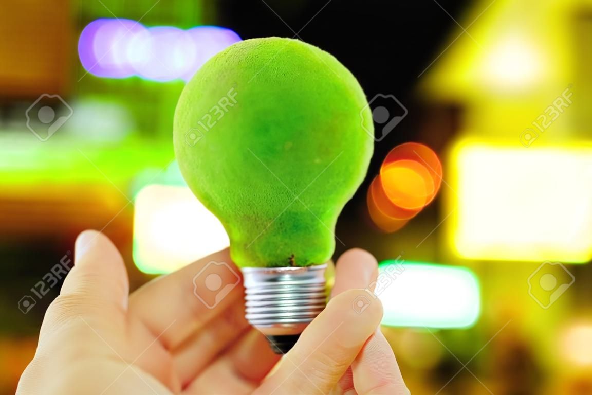 hand holding green light bulb and defocused city night light background, eco energy concept