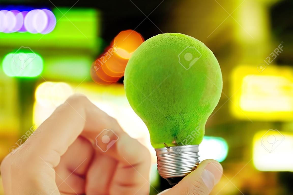 hand holding green light bulb and defocused city night light background, eco energy concept