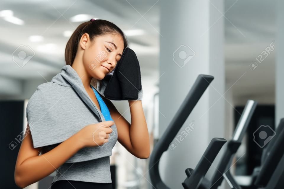 Vermoeide jonge vrouw veegt haar zweet af na training in de sportschool.