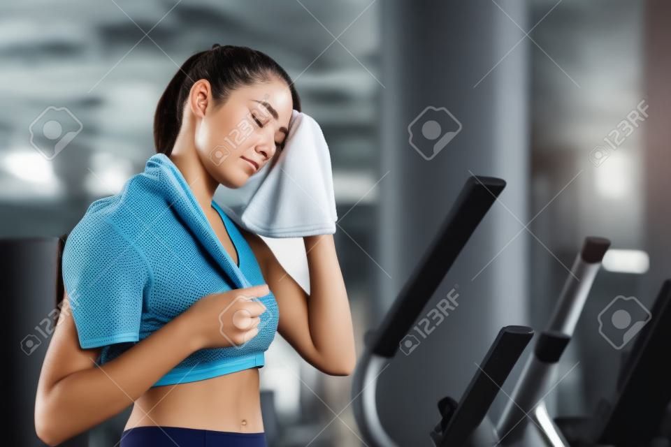 疲れた若い女性は、ジムでの運動トレーニングの後に汗を拭いています。