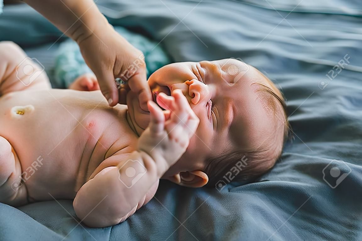 Bebé recién nacido blanco con cabello rubio usando pañal acostado en una cama azul llorando mientras su madre lo cambia, cuidando a un bebé, toma horizontal en interiores, foto de alta calidad