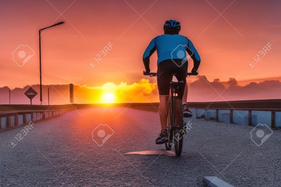 Ciclista la bici in piedi sul sentiero roccioso della montagna al tramonto, turista con lo zaino