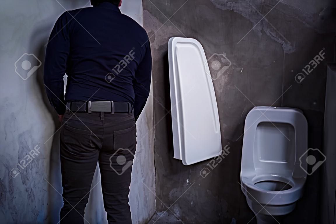 Przystojny mężczyzna sika do muszli klozetowej w toalecie. pisuary w białej toalecie publicznej