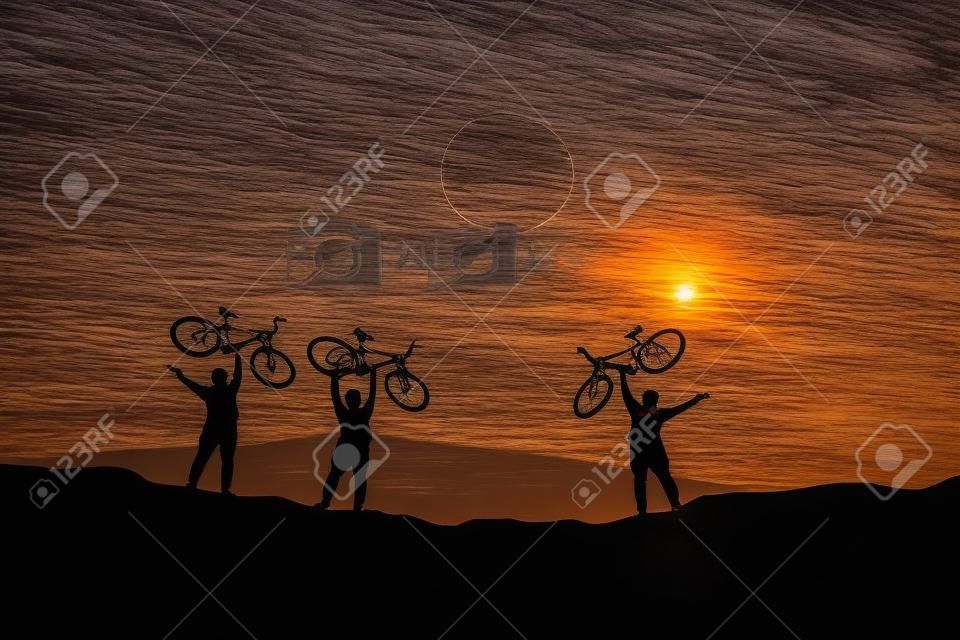 Silhouettes of touring cyclists practicing in the mountains offer beautiful views in the evening.
Adventure tourists by bicycle. adventure concept. Silhouettes of 3 men happily raising bicycles in the evening.