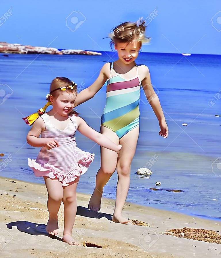 Niños tomados de la mano, caminando en la playa. Vista posterior.