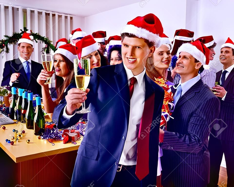 Рождественский бизнес-коктейль в офисе. Рождественский корпоратив с группой людей в праздничной шляпе, пьющей шампанское.