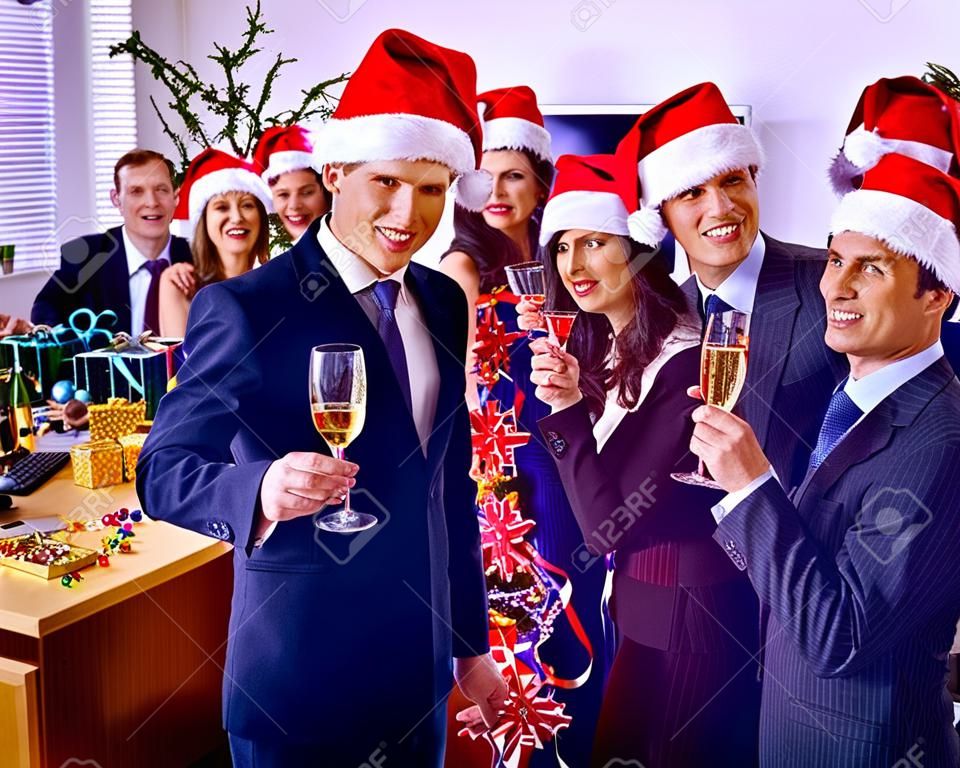 Рождественский бизнес-коктейль в офисе. Рождественский корпоратив с группой людей в праздничной шляпе, пьющей шампанское.