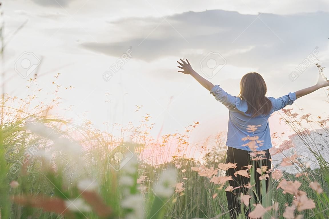 Young beautiful woman standing stretch her arms in the air on the grass field. Woman enjoy with nature during sunset.