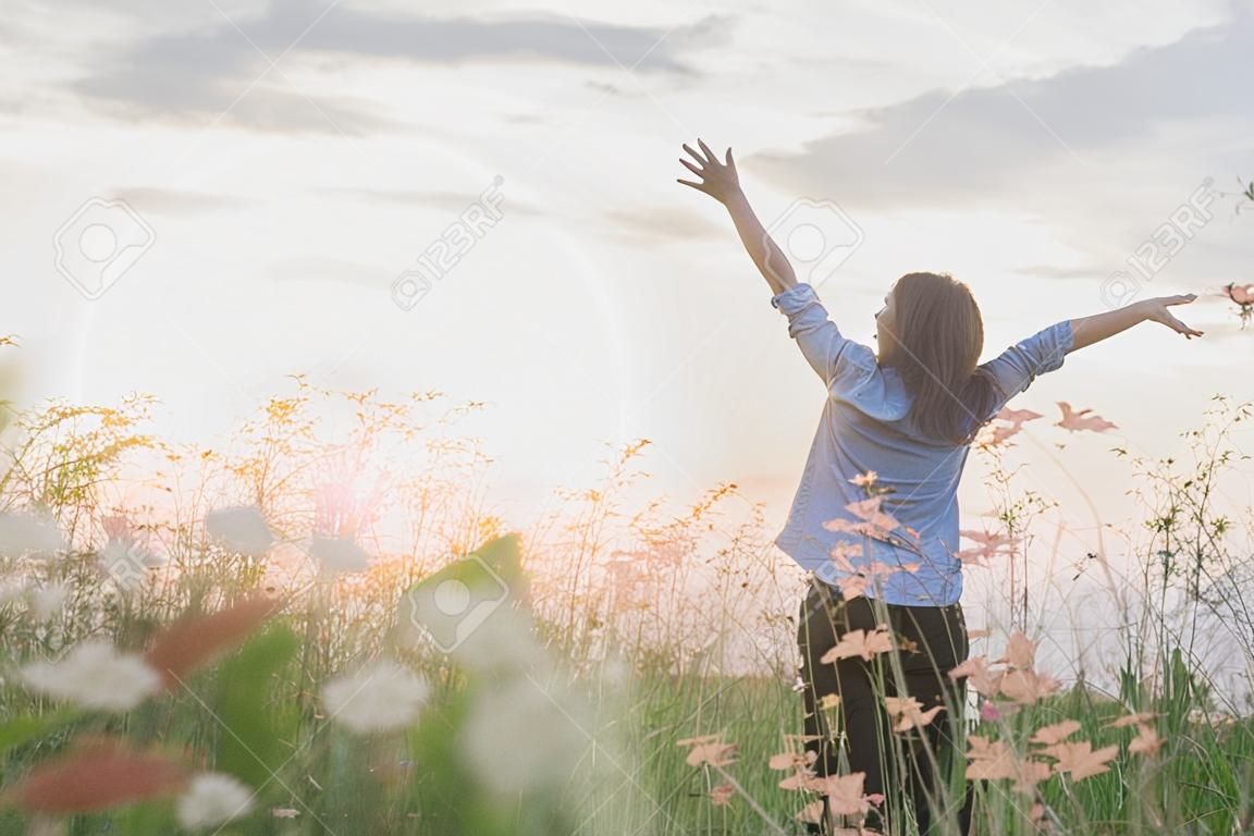 Young beautiful woman standing stretch her arms in the air on the grass field. Woman enjoy with nature during sunset.