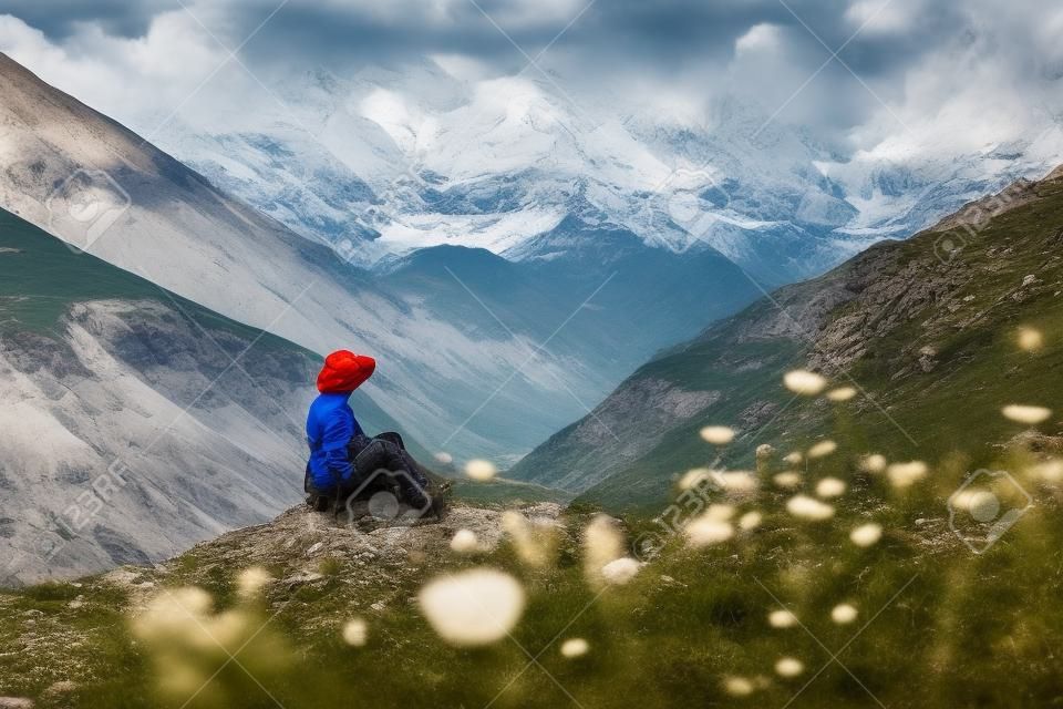 Tourist sitting on the rock at green pasture against highest georgian mountain Shkhara near Ushguli in Georgia.
