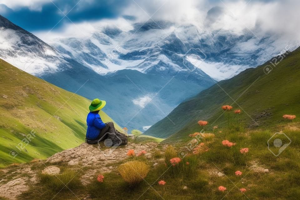 Tourist sitting on the rock at green pasture against highest georgian mountain Shkhara near Ushguli in Georgia.