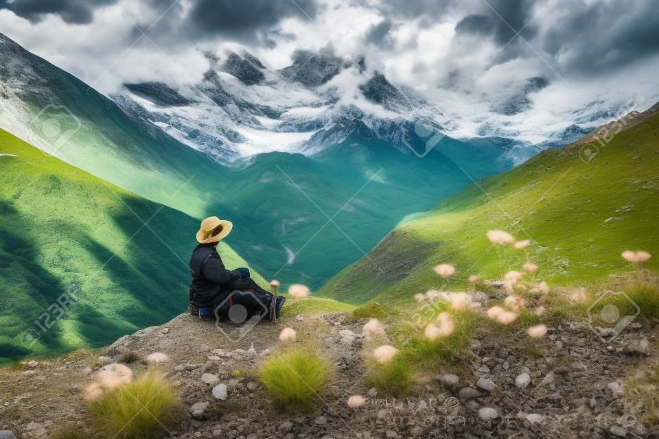 Turysta siedzący na skale na zielonych pastwiskach przed najwyższą gruzińską górą shkhara w pobliżu ushguli w gruzji.