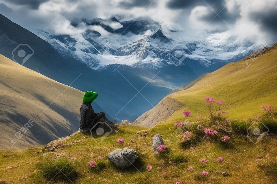 Turysta siedzący na skale na zielonych pastwiskach przed najwyższą gruzińską górą shkhara w pobliżu ushguli w gruzji.