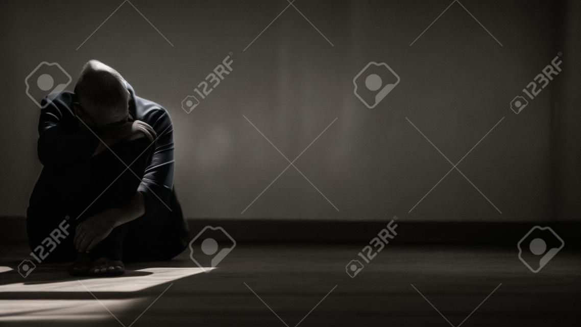 Luz solar e sombra na superfície do homem sem esperança sentado sozinho com abraçando os joelhos no chão no quarto escuro vazio em estilo preto e branco