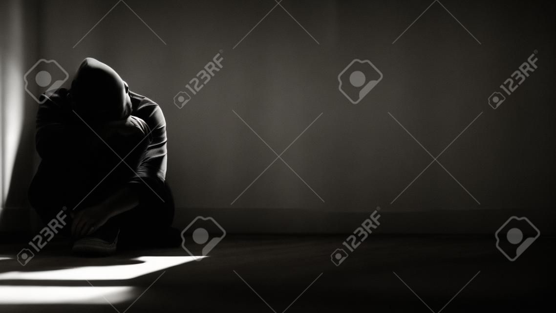 Luz solar e sombra na superfície do homem sem esperança sentado sozinho com abraçando os joelhos no chão no quarto escuro vazio em estilo preto e branco