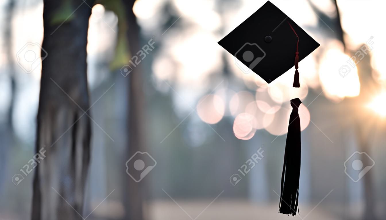 Mano de mujer graduada sosteniendo el gorro de graduación en su mano sobre fondo de bosque borroso. Concepto de celebración de graduación.