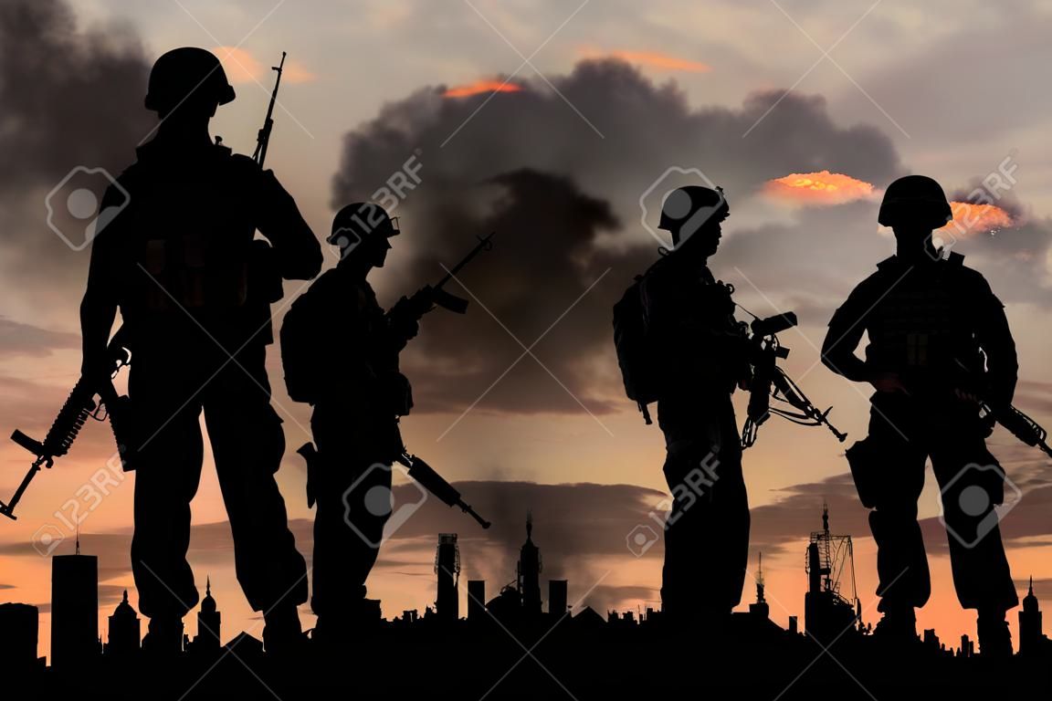 concept of war. Silhouettes of military soldiers with weapons against the backdrop of the city in the smoke and explosions