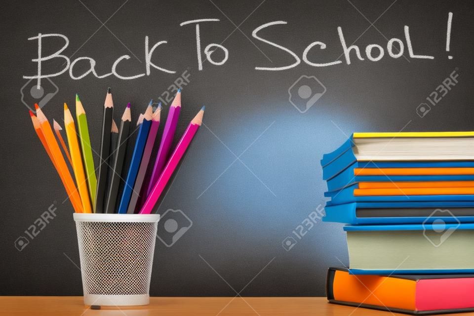 Stack of colorful textbooks and copybooks with pencils near by on background of blackboard