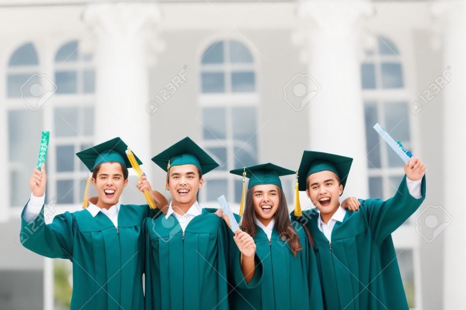 Group of smart students in graduation gowns holding diplomas