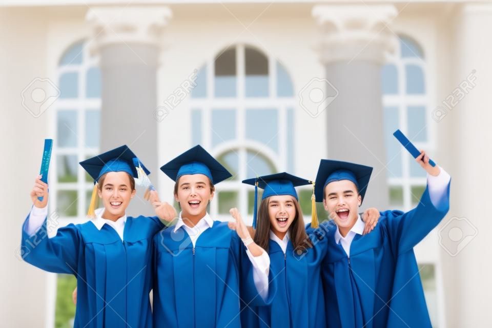 Group of smart students in graduation gowns holding diplomas