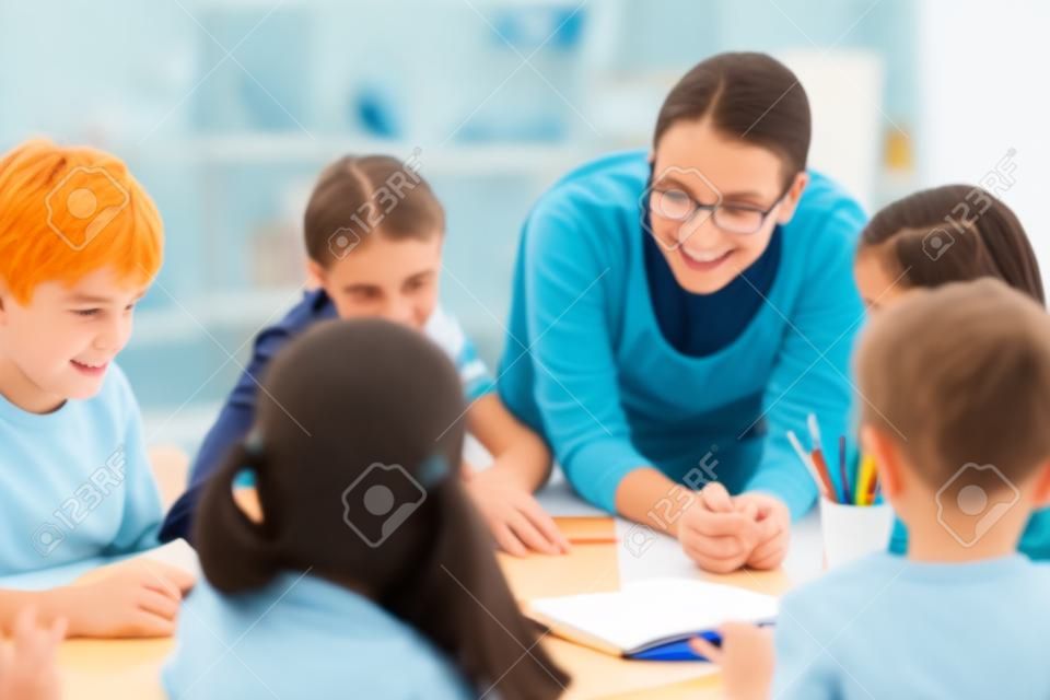 Retrato de escolares diligentes y su maestra hablando en la lección