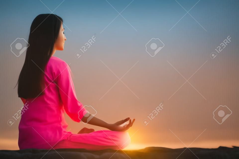 沉思的女子坐在蓮花反對晴朗的天空的姿勢戶外側視圖