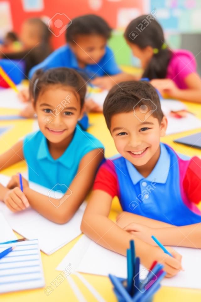 Two schoolkids looking at camera while drawing on background of little girls