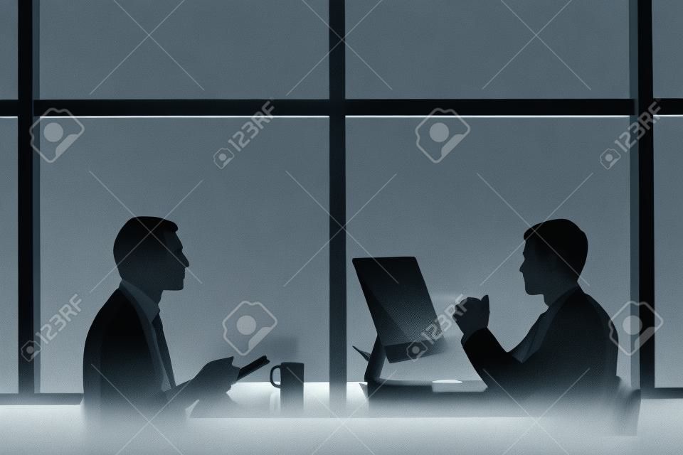 Contornos de dos hombres de negocios trabajando hasta tarde en la oficina