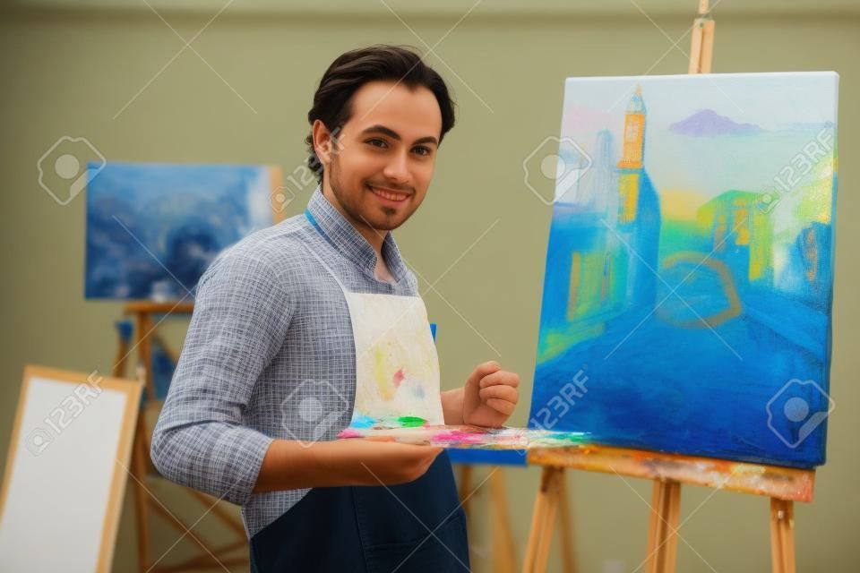 Young artist looking at camera on background of his painting