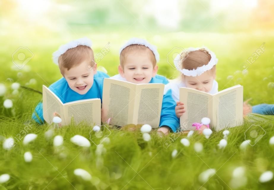 Cute children in dandelion wreaths reading on lawn