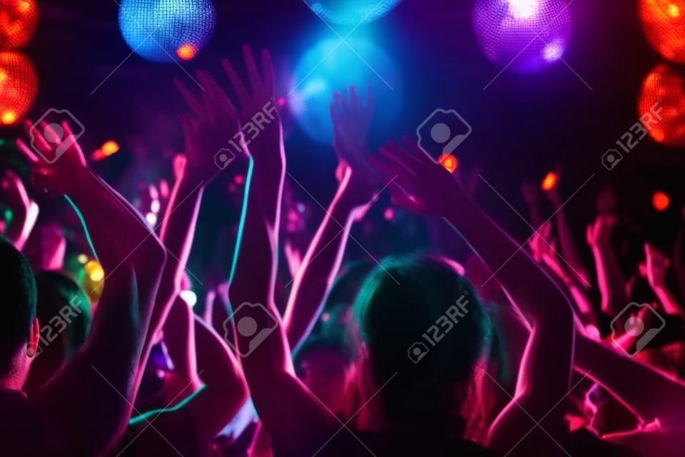 Multitud de personas con los brazos levantados bailando en club nocturno